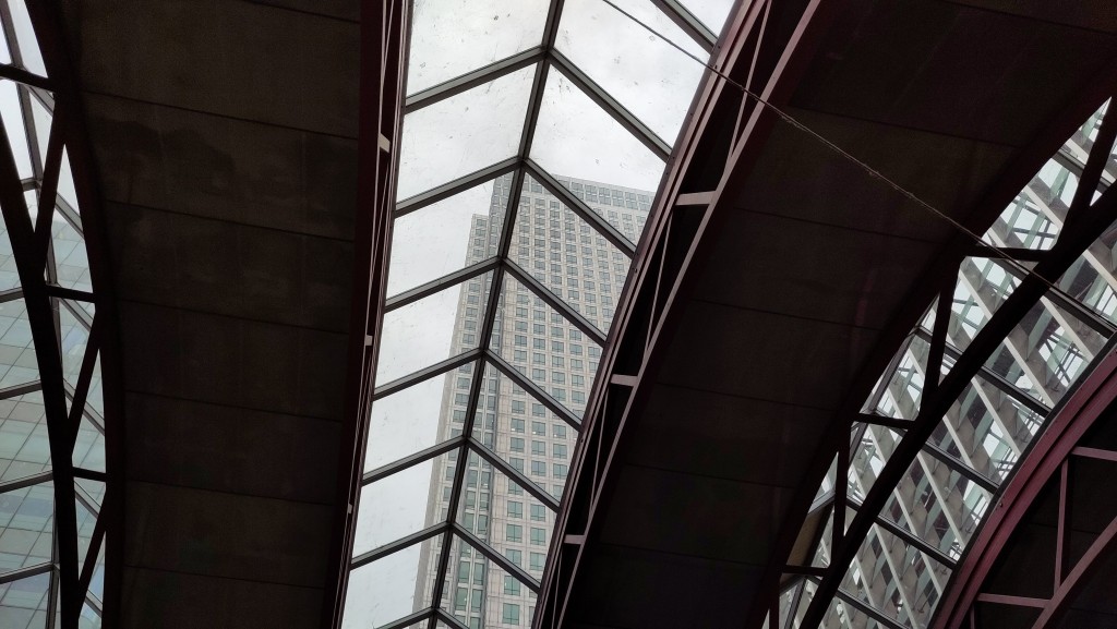 View through a partially glazed, vaulted roof to a skyscraper with many floors of windows in a grid
